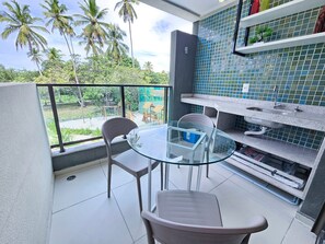 A balcony with a glass table and chairs, a sink, and a view of palm trees.