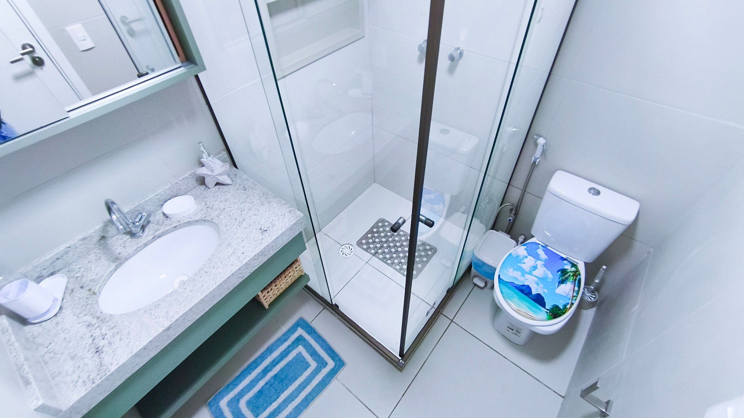 A bathroom with a glass shower enclosure, a sink with a mirror, and a toilet with a decorative cover.