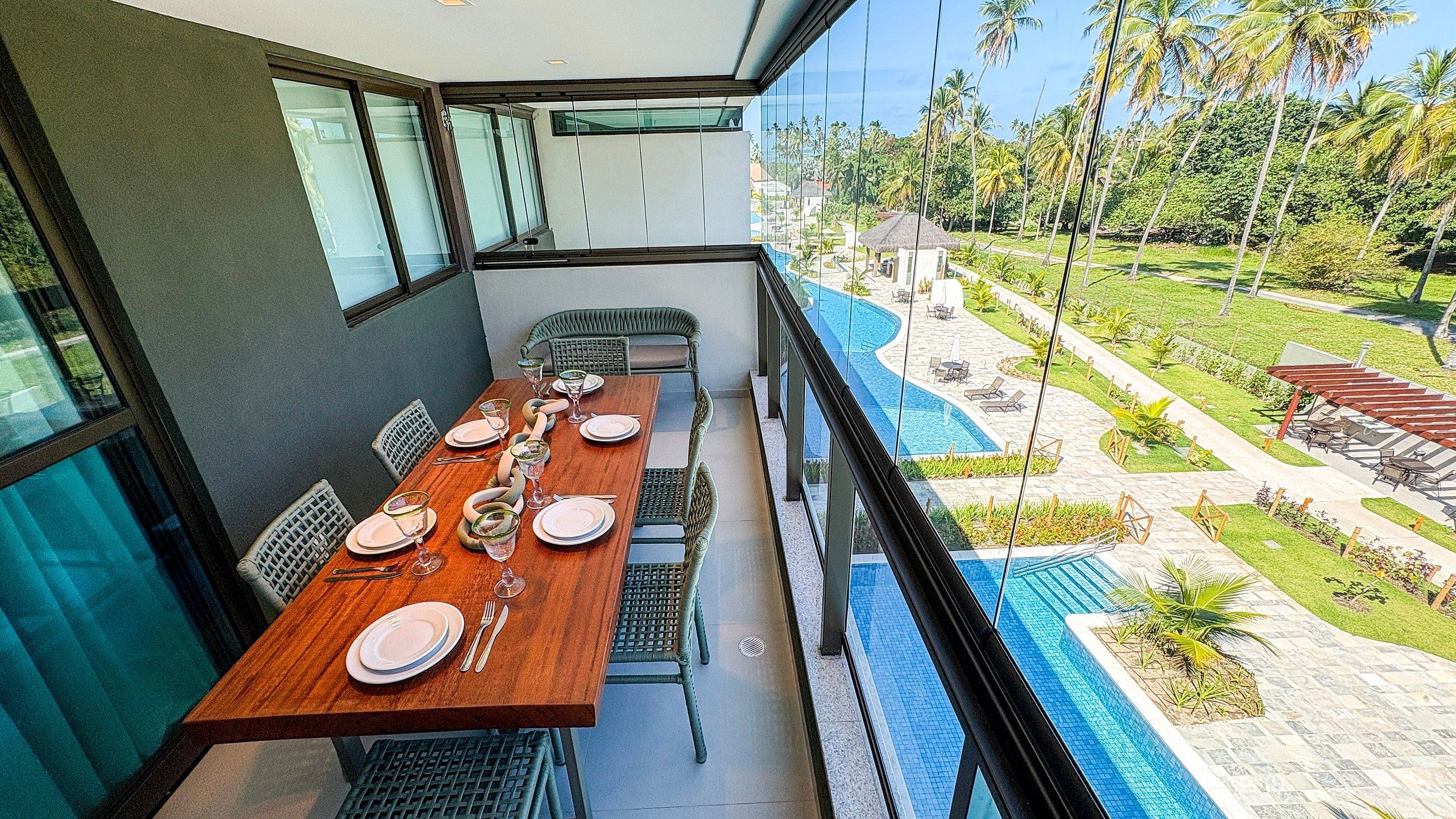 Comedor con una larga mesa dispuesta para cuatro, con vista a una piscina y un jardín.