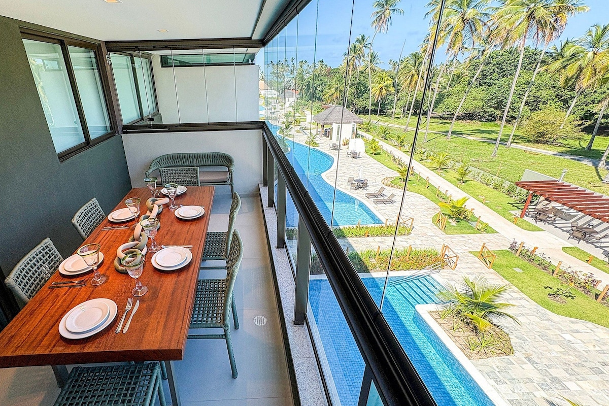 A dining area with a long table set for four, overlooking a pool and garden.