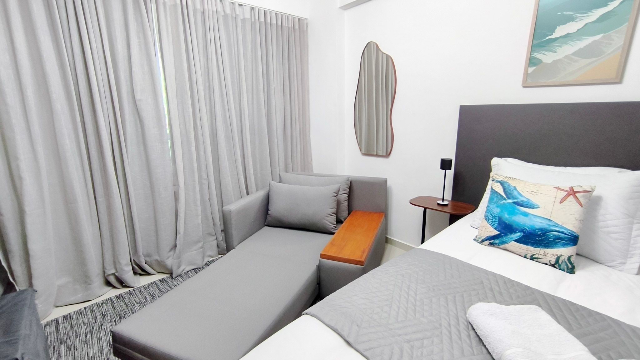 A hotel room with a bed, a sofa, a small table, a lamp, and a painting on the wall.