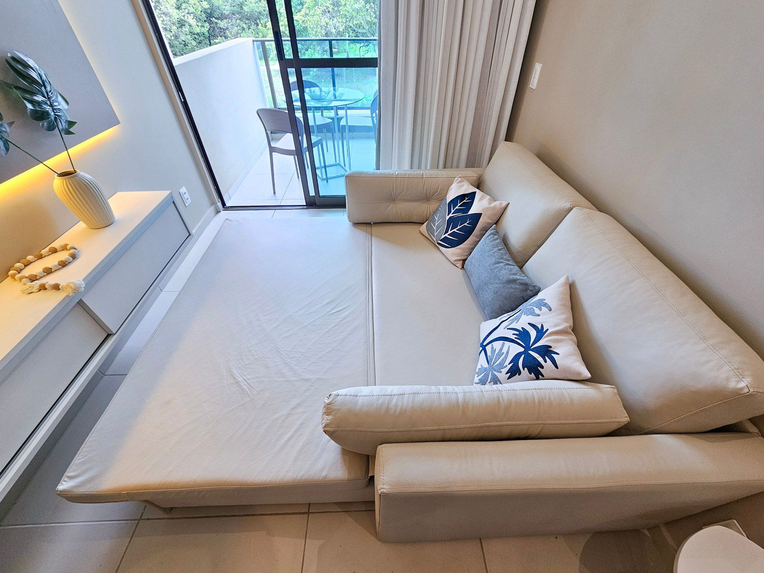 A modern living room with a sofa, pillows, a small table with a plant, and a view of an outdoor patio.