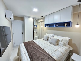 Un dormitorio con cama, mesitas de noche, armario, espejo y estante con objetos decorativos.