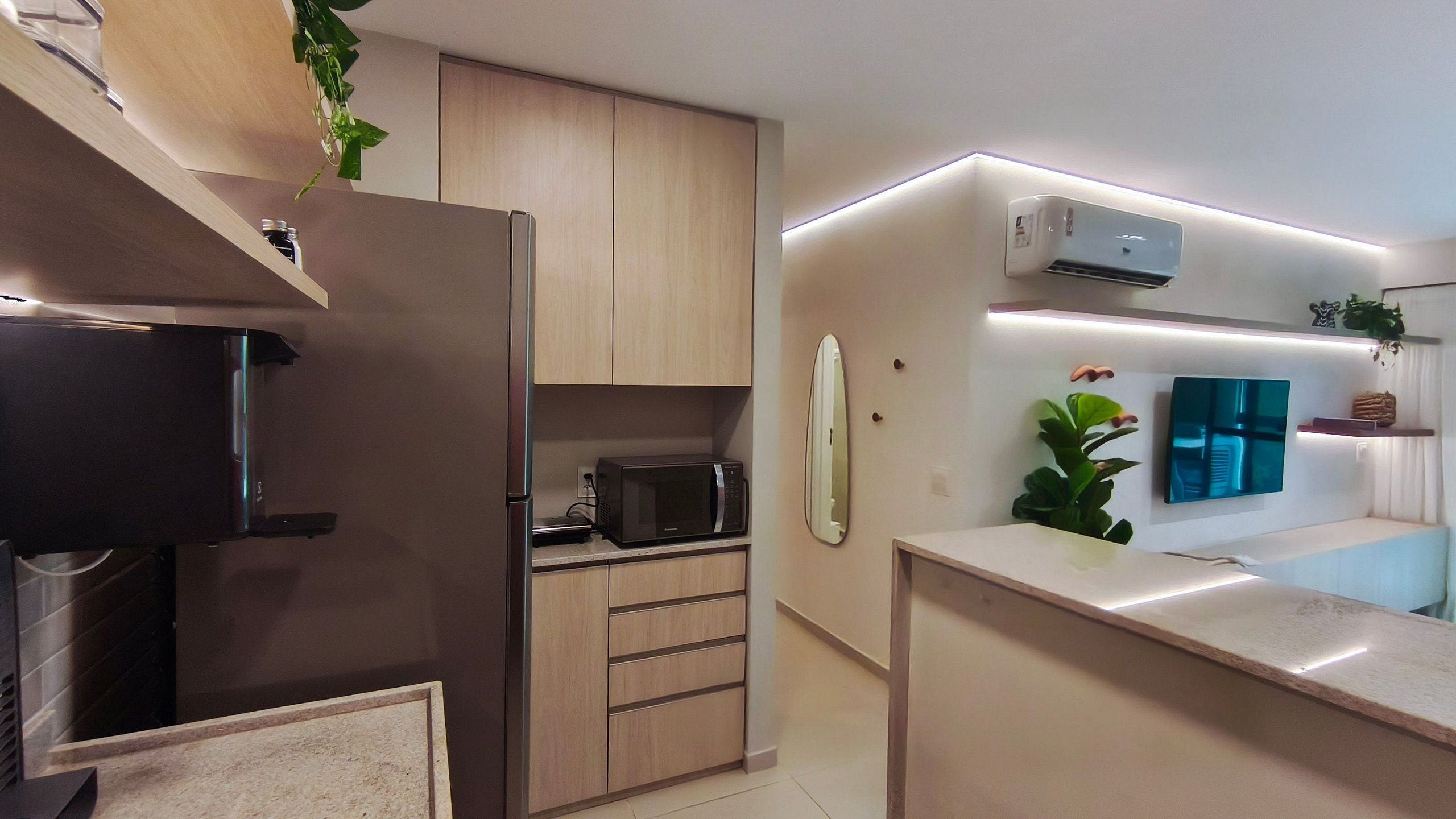 A modern kitchen with a built-in microwave, a refrigerator, and a flat-screen TV mounted on the wall.