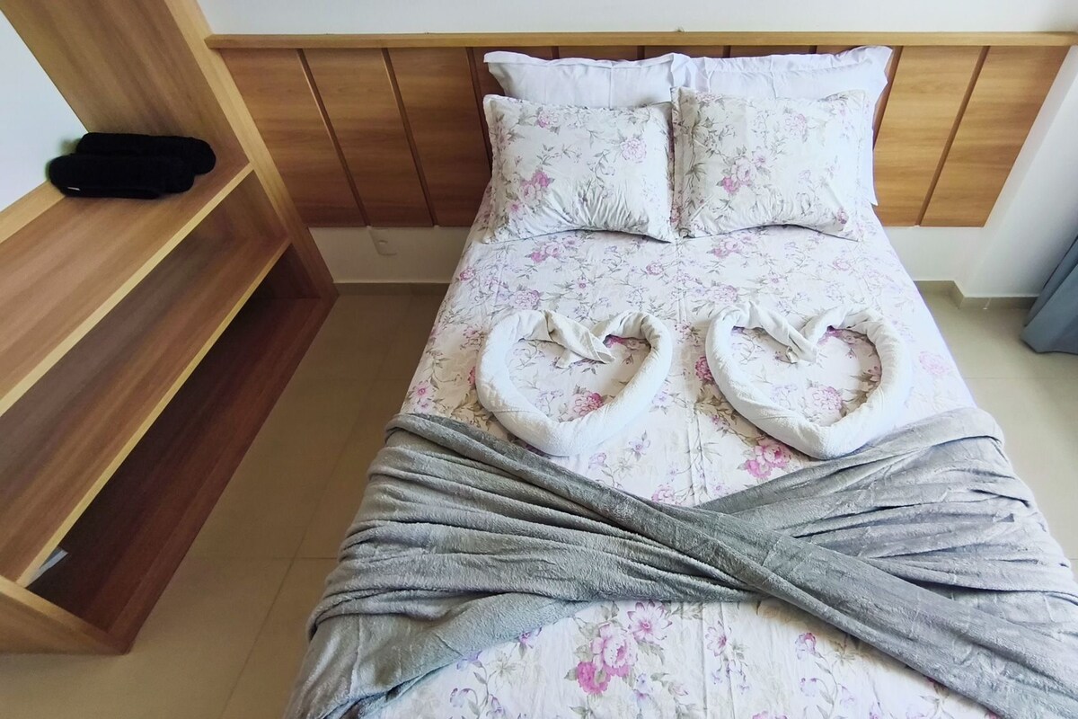 Una cama individual con ropa de cama floral, un edredón gris y un cabecero de madera.