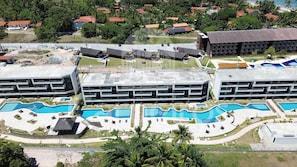 A resort with multiple swimming pools, a large building with a unique roof design, and surrounding greenery. - Galapagos Beach Residence - Praia dos Carneiros (Tamandaré)