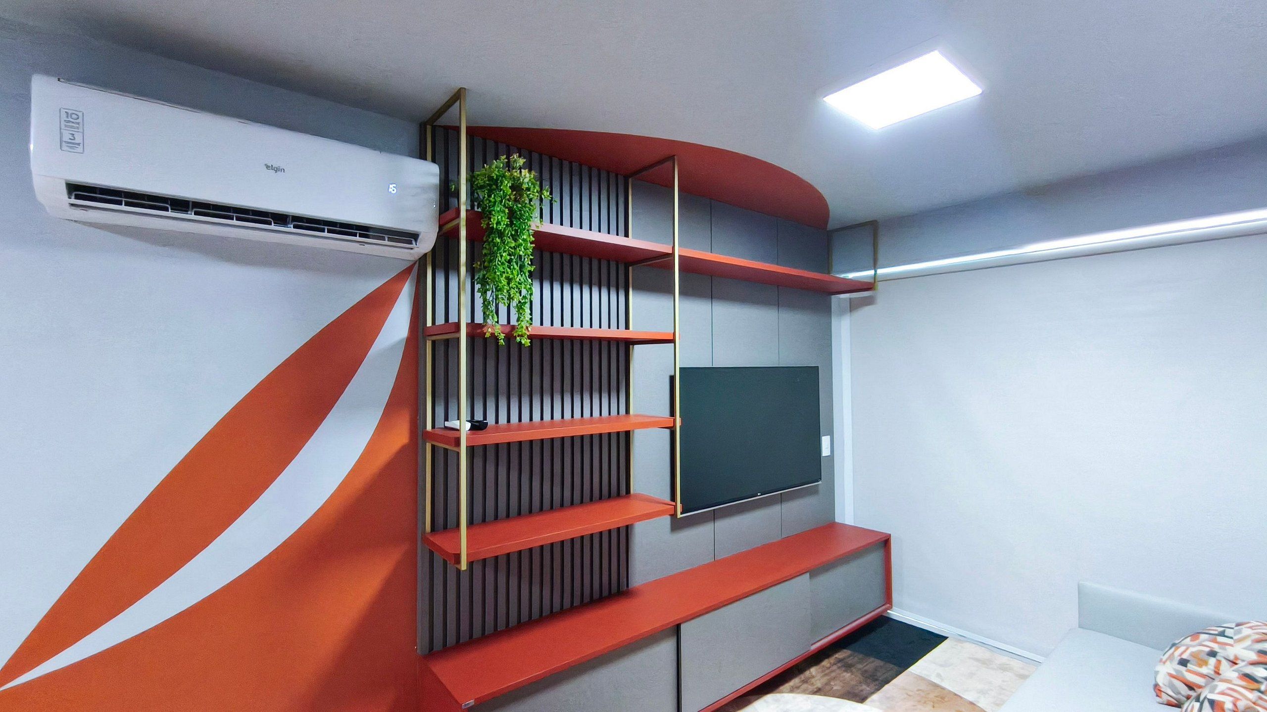 A modern living room with a built-in TV, a red and grey shelving unit, and a potted plant.