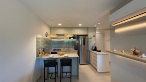 A modern kitchen with a central island, two bar stools, a stainless steel refrigerator, and a microwave above the island. - Galapagos Beach Residence - Praia dos Carneiros (Tamandaré)