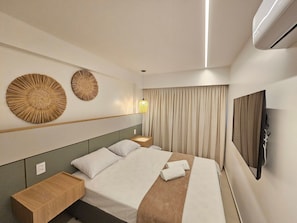 A hotel room with a bed, bedside tables, a wall-mounted TV, and decorative wall art.
