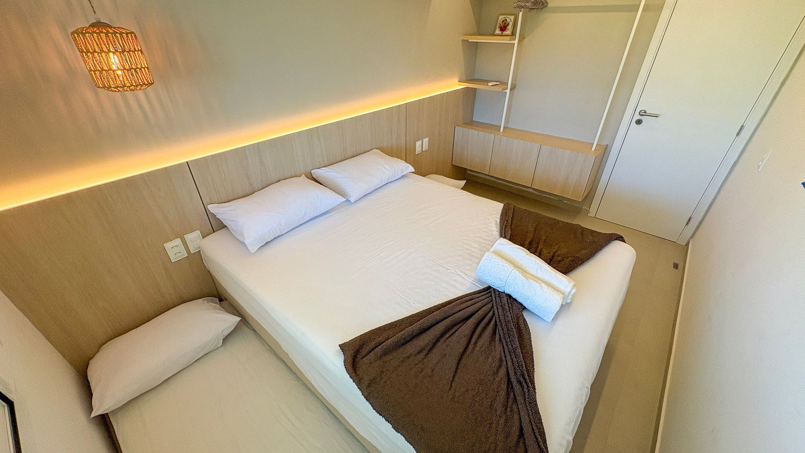 A compact hotel room with a bed, bedside tables, a wardrobe, and a wall-mounted light fixture.