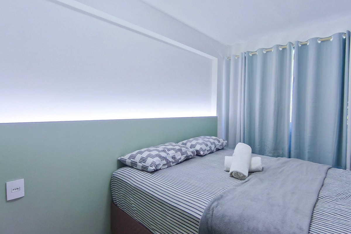 Ein Einzelbett mit gestreifter Bettwäsche, einem Kopfkissen und einer Decke. Eine Steckdose ist an der Wand vorhanden.