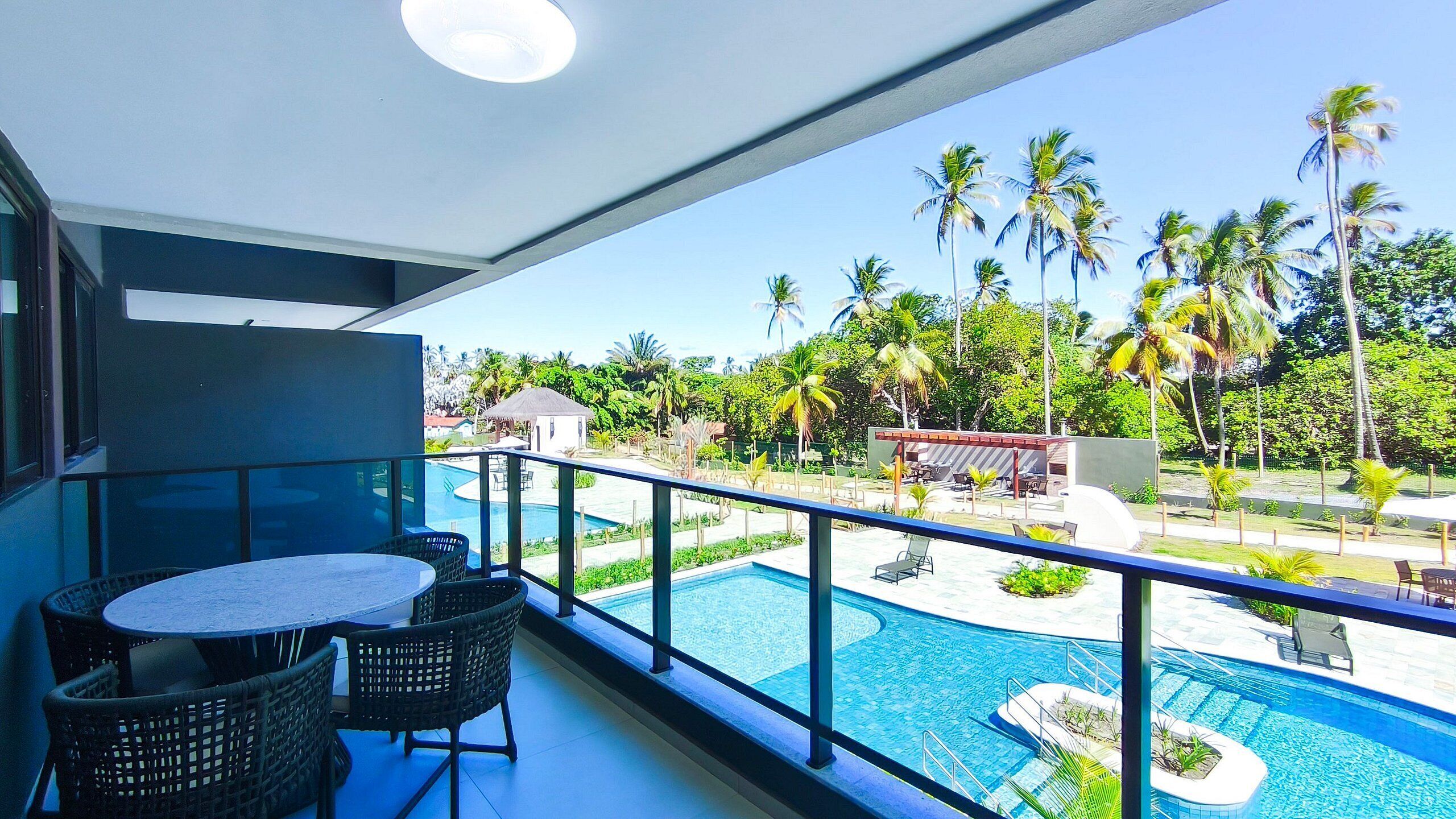 A balcony with a table and chairs, overlooking a swimming pool and palm trees.