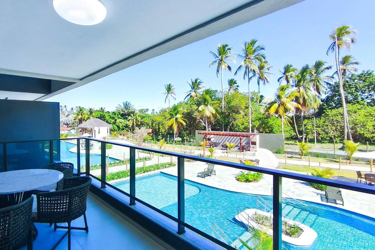 Un balcón con mesa y sillas, con vistas a una piscina y palmeras.