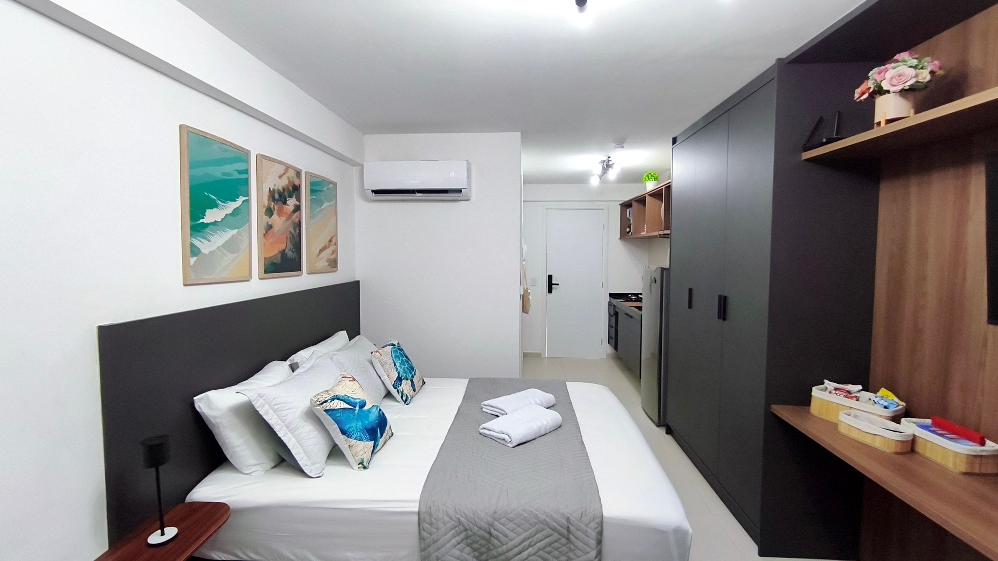Ein Hotelzimmer mit Bett, Nachttisch, Kleiderschrank, einer kleinen Küchenzeile und Wandbildern.