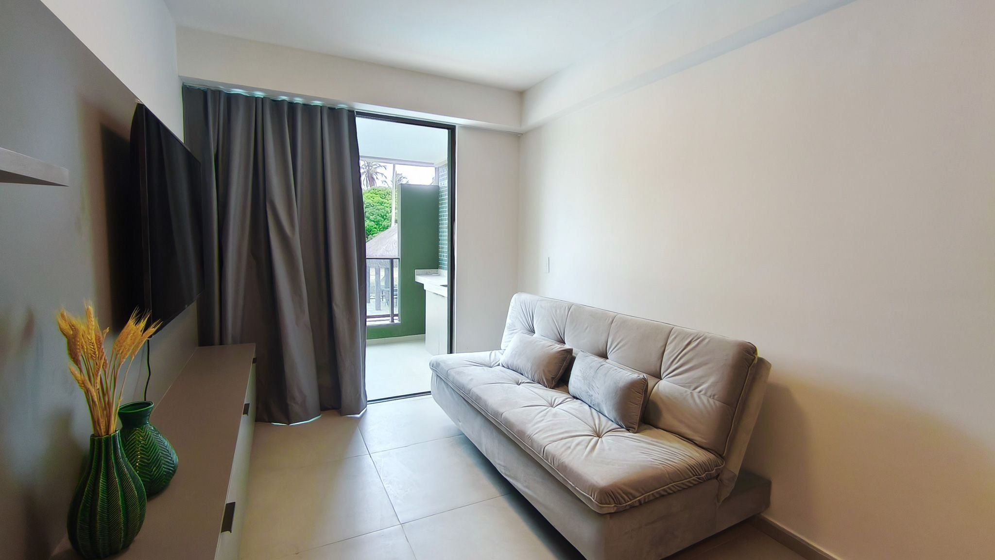 A modern living room with a sofa, a flat-screen TV, and a sliding glass door leading to an outdoor area.