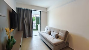 A modern living room with a sofa, a flat-screen TV, and a sliding glass door leading to an outdoor area.