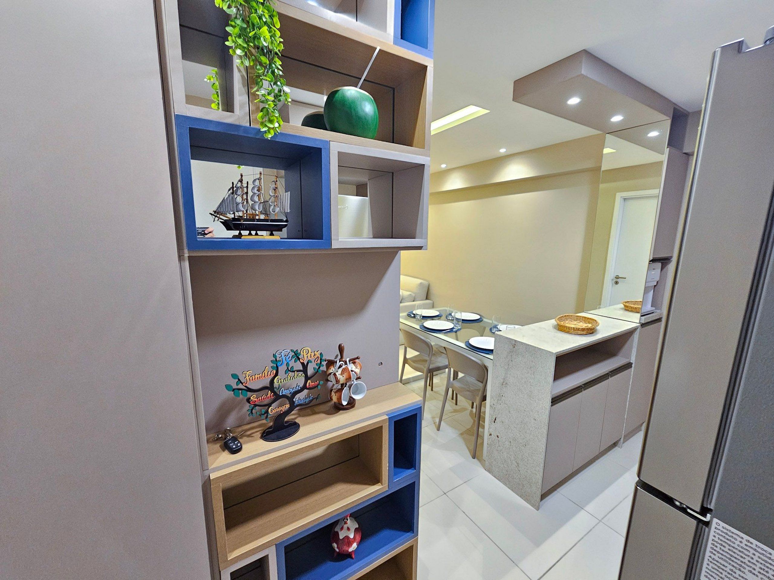 A modern kitchen with built-in shelves, a dining area with a table set for two, and a refrigerator.