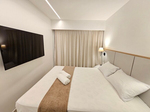 A hotel room with a bed, a TV mounted on the wall, a bedside lamp, and a window with curtains. - Galapagos Beach Residence - Praia dos Carneiros (Tamandaré)