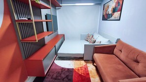 A compact room with a sofa, a small bed, a built-in shelf unit, and a colorful rug. - Galapagos Beach Residence - Praia dos Carneiros (Tamandaré)