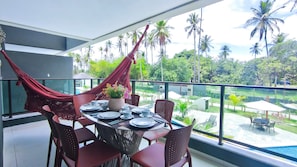 A dining area with a table set for four, a hammock, and a view of a swimming pool and palm trees. - Galapagos Beach Residence - Praia dos Carneiros (Tamandaré)