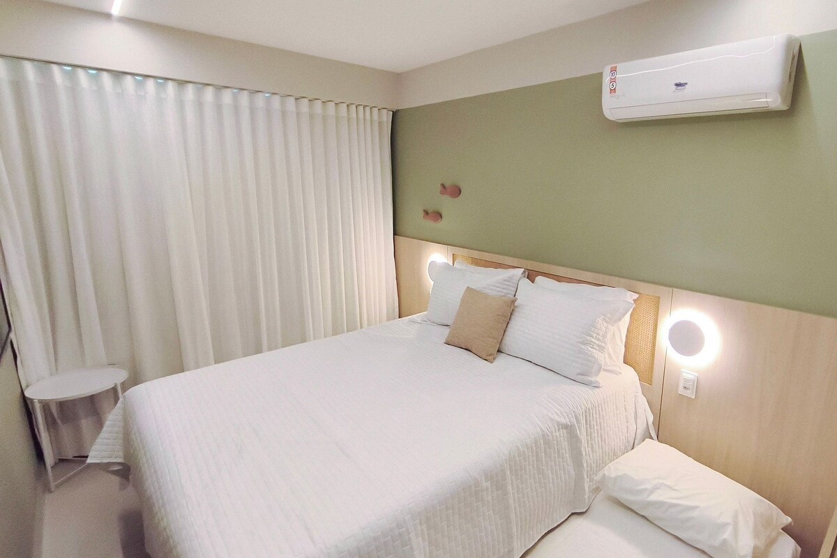 Habitación de hotel con cama, mesita de noche, aire acondicionado de pared y ventana con cortinas.