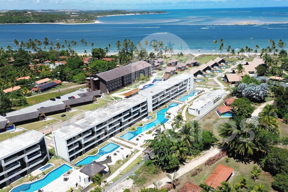 A resort with multiple swimming pools, a large building, and a view of the ocean.