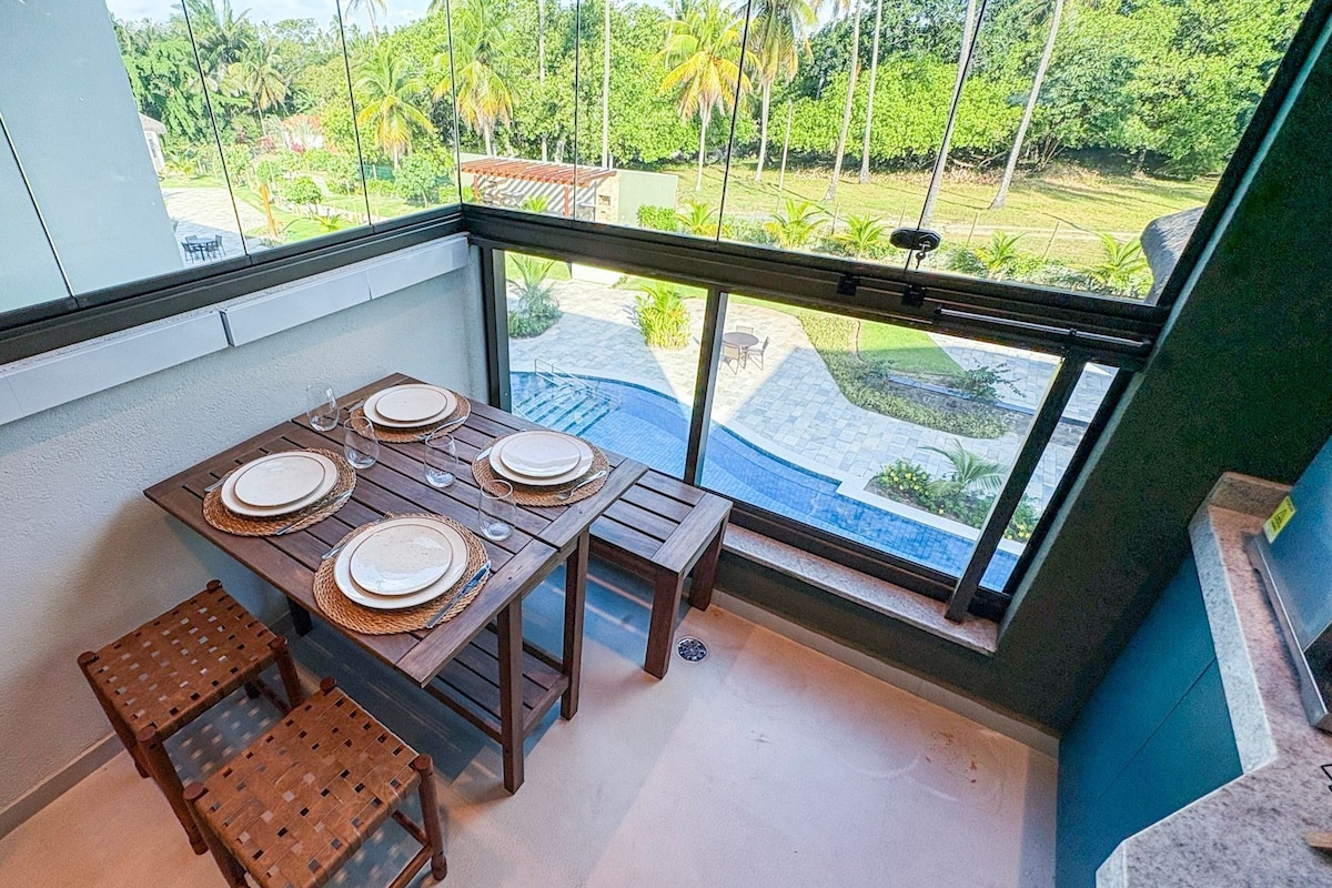 A balcony with a table set for four, overlooking a lush garden and a swimming pool.