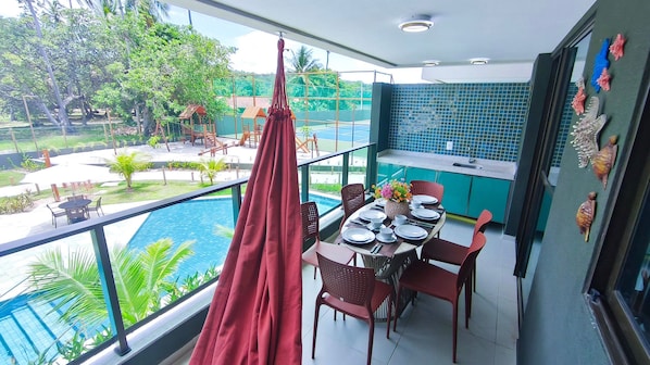 A balcony with a dining table set for four, overlooking a swimming pool and lush greenery. - Galapagos Beach Residence - Praia dos Carneiros (Tamandaré)