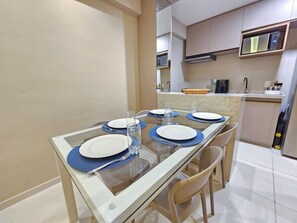 A dining area with a glass table, blue placemats, white plates, and clear glasses.