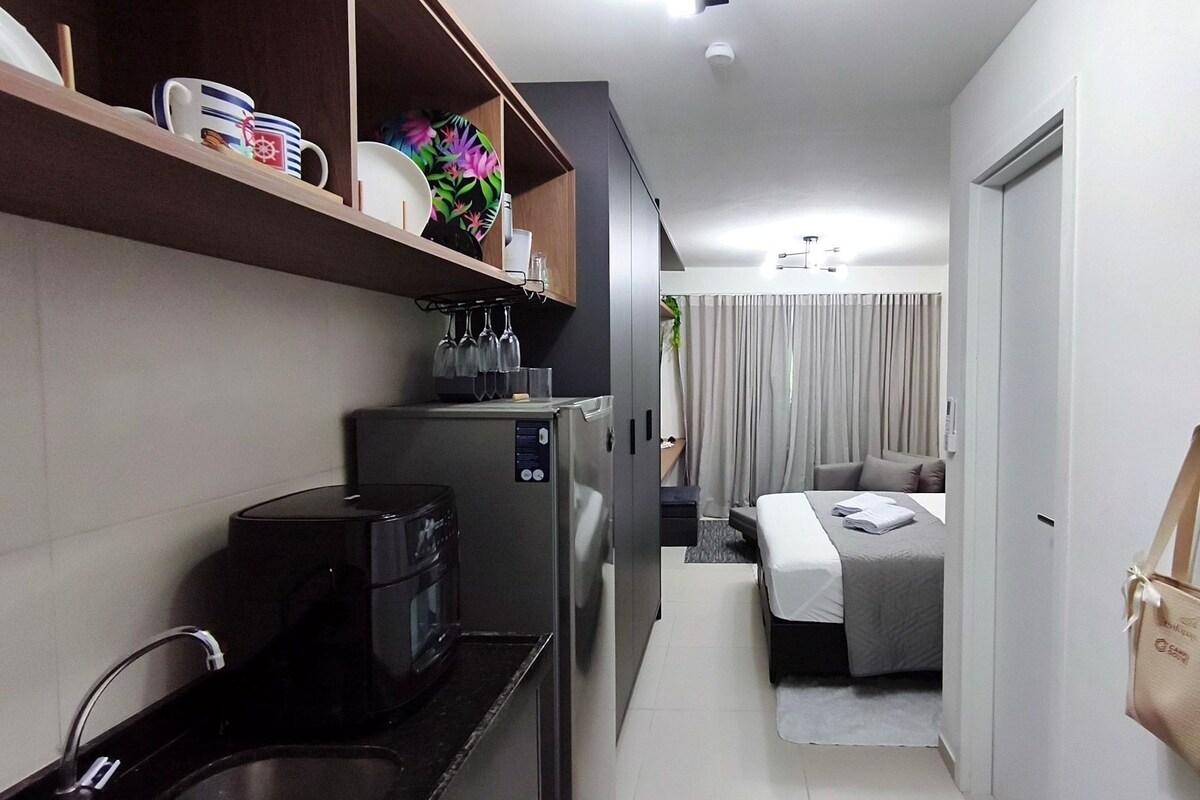 A compact hotel room with a kitchenette, a bed, a small seating area, and a bathroom.