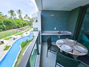 A balcony with a view of a swimming pool, a dining table set with plates and glasses, and a tiled backsplash. - Galapagos Beach Residence - Praia dos Carneiros (Tamandaré)