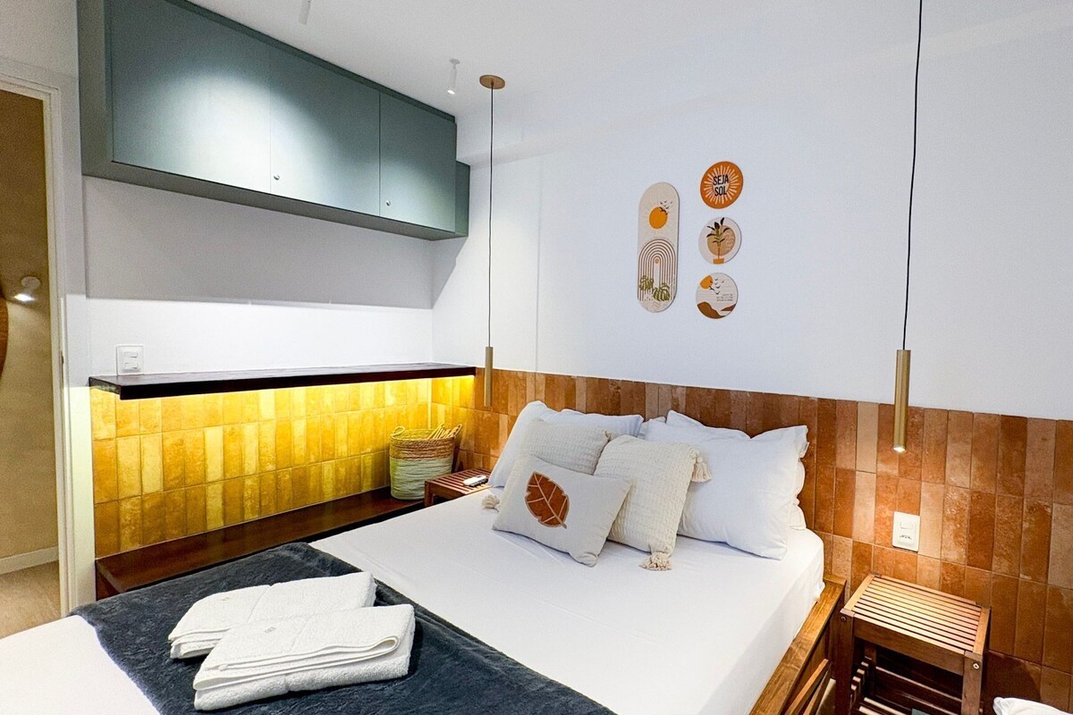 A modern hotel room with a bed, a small bedside table, a wall-mounted cabinet, and a wall with decorative items.