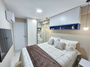 A bedroom with a bed, bedside tables, a wardrobe, a mirror, and a shelf with decorative items. - Galapagos Beach Residence - Praia dos Carneiros (Tamandaré)