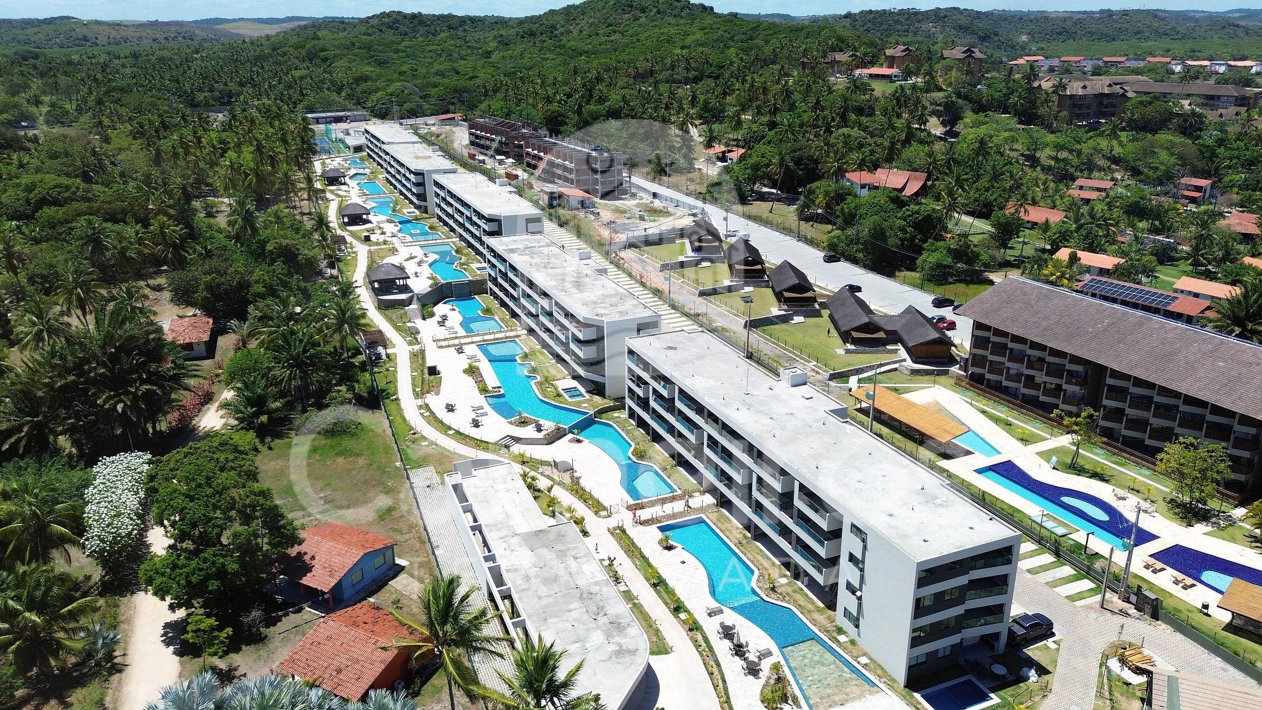 Ein Resort mit mehreren Schwimmbecken, einem großen Gebäude mit Balkonen und einer üppigen, grünen Umgebung.