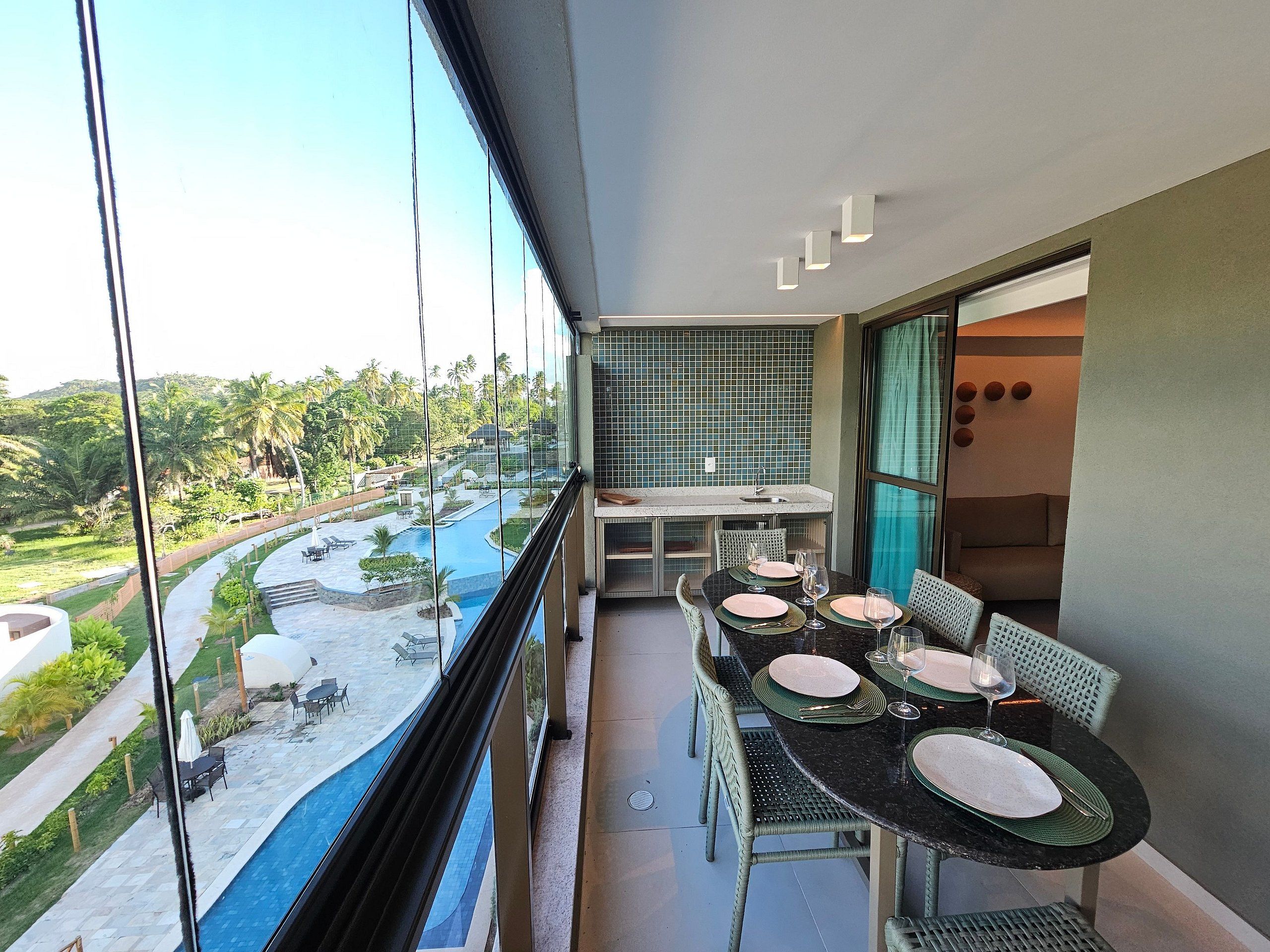Un balcon avec une table à manger pour deux personnes, donnant sur une piscine et une végétation luxuriante.