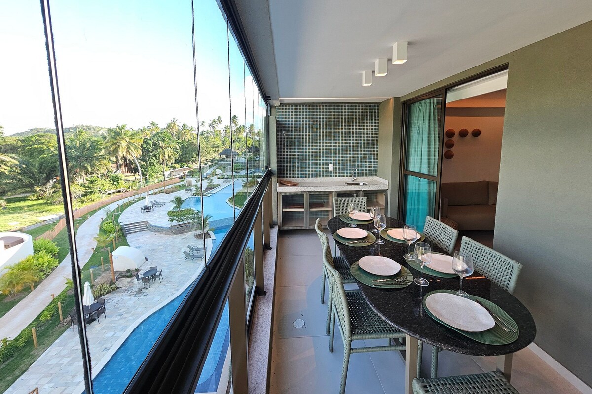 A balcony with a dining table set for two, overlooking a pool and lush greenery.