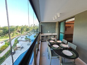 A balcony with a dining table set for two, overlooking a pool and lush greenery.
