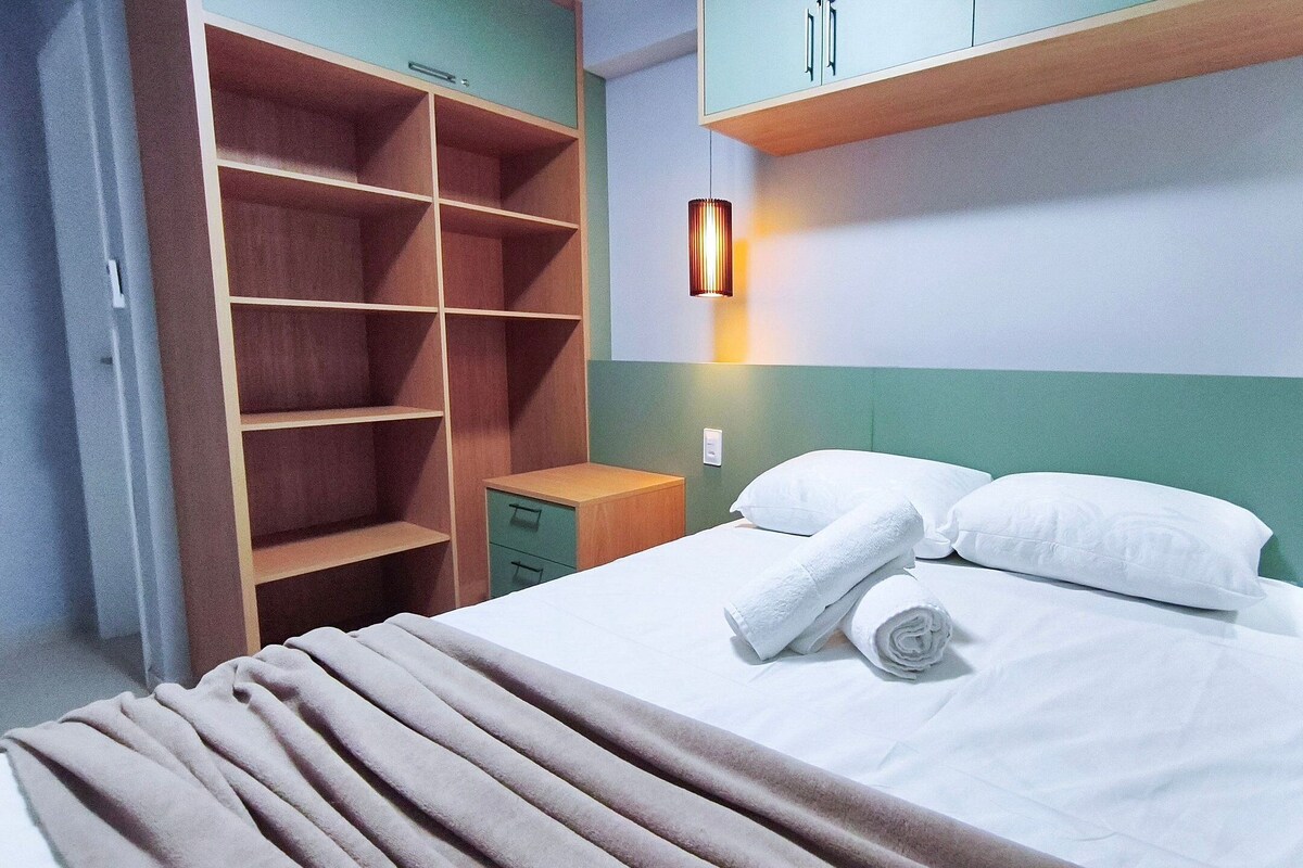 A hotel room with a bed, a nightstand, a wardrobe, and a wall-mounted light.