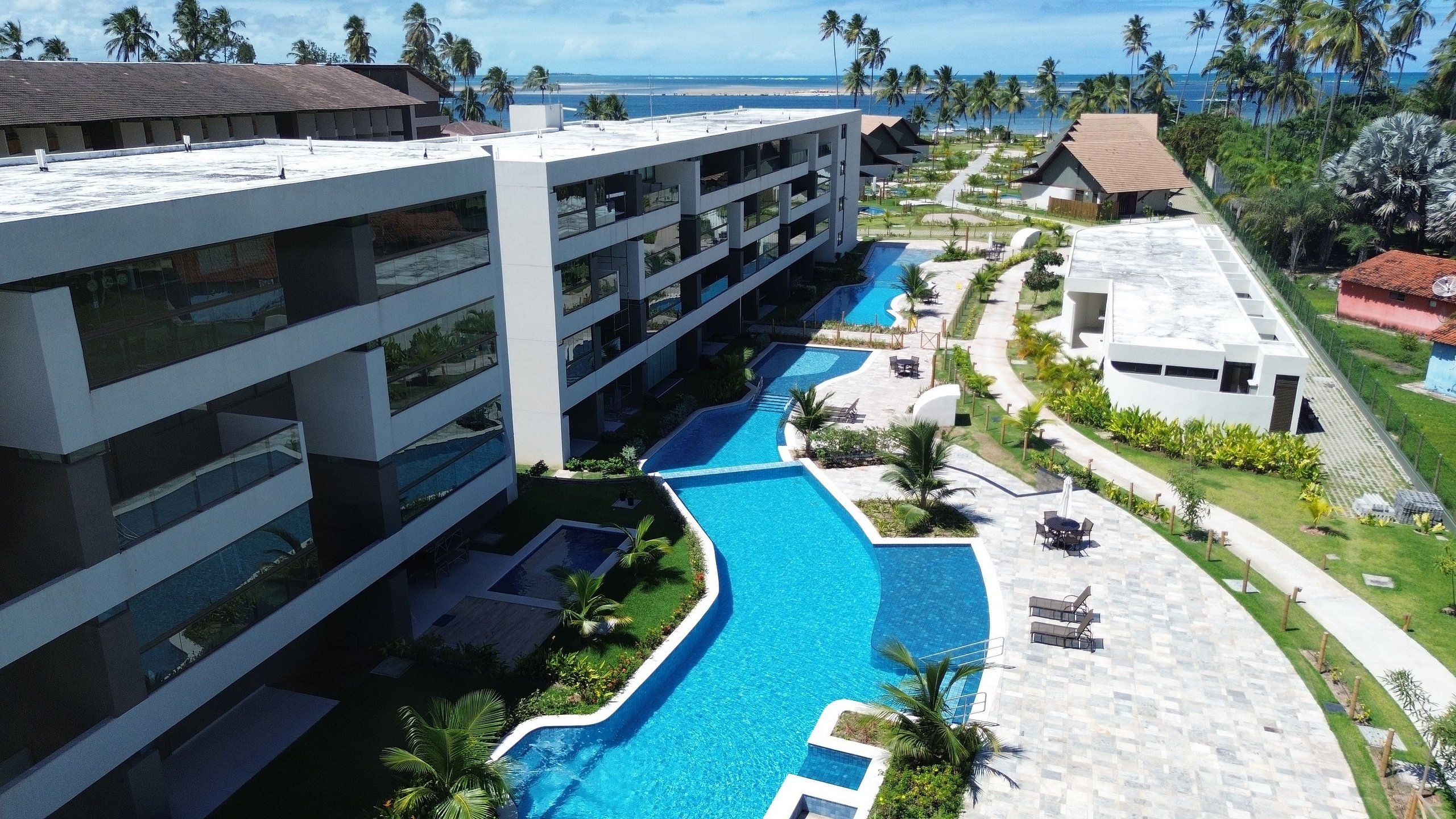 A resort with a swimming pool, multiple buildings, and a view of the ocean.