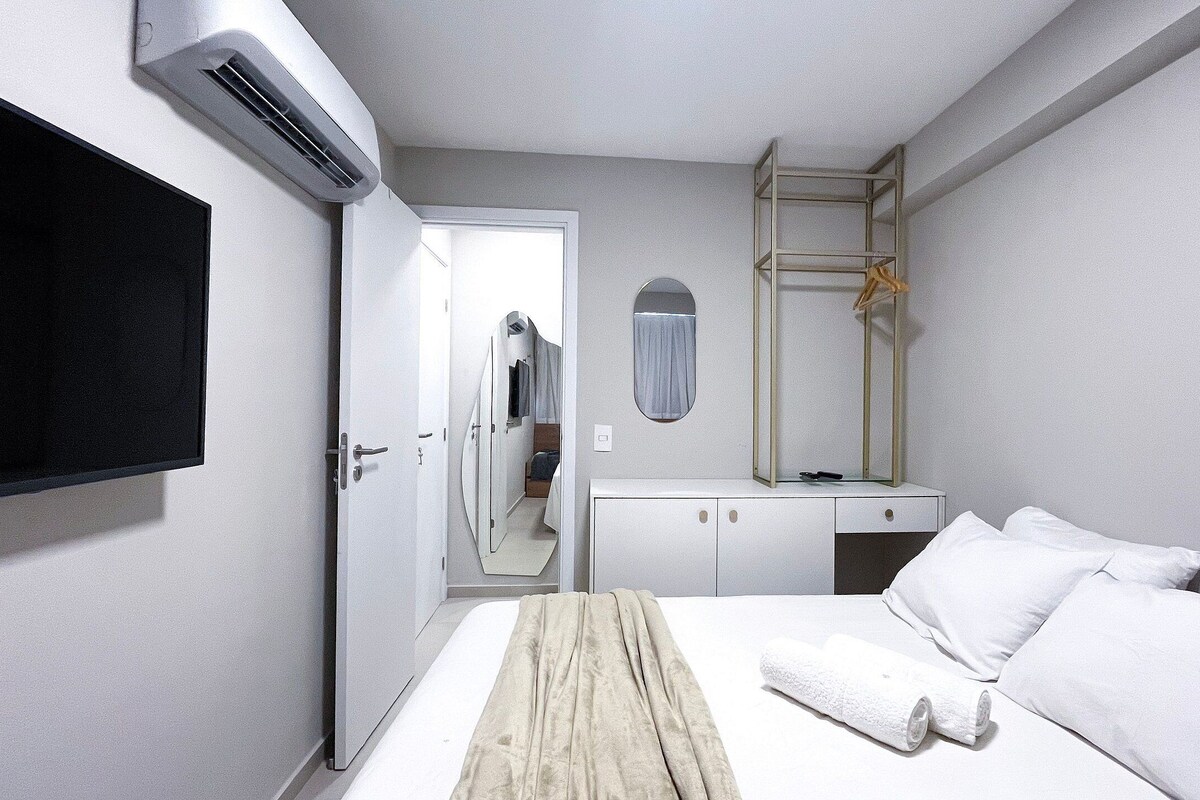 A hotel room with a bed, a TV, a wardrobe, a mirror, and an air conditioning unit.