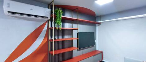 A modern living room with a built-in TV, a red and grey shelving unit, and a potted plant.