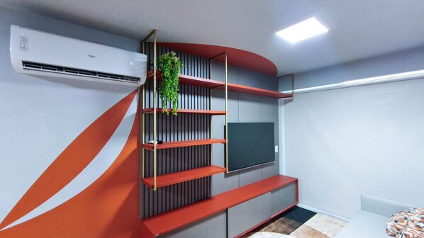 A modern living room with a built-in TV, a red and grey shelving unit, and a potted plant. - Galapagos Beach Residence - Praia dos Carneiros (Tamandaré)
