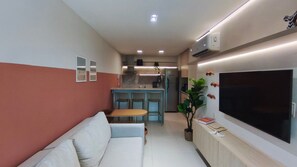 A compact living space with a sofa, a dining table, a TV, a kitchen area, and a potted plant. - Galapagos Beach Residence - Praia dos Carneiros (Tamandaré)