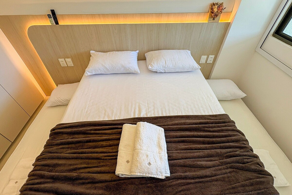 Una habitación de hotel con cama, almohadas, una manta y ventana.