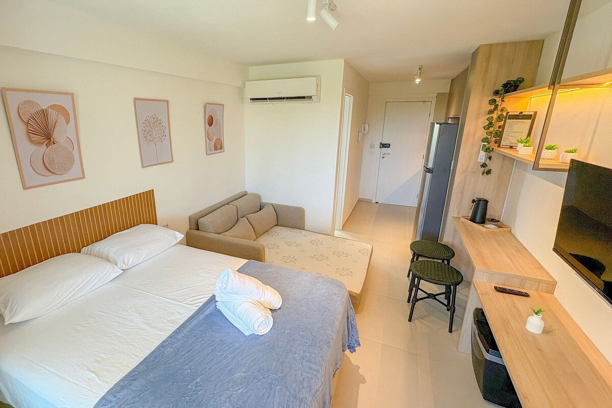 A hotel room with a bed, a sofa, a TV, and a kitchen area.