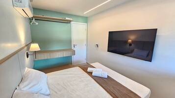 A hotel room with a bed, a mounted TV, a wall-mounted air conditioner, and a towel on the bed.