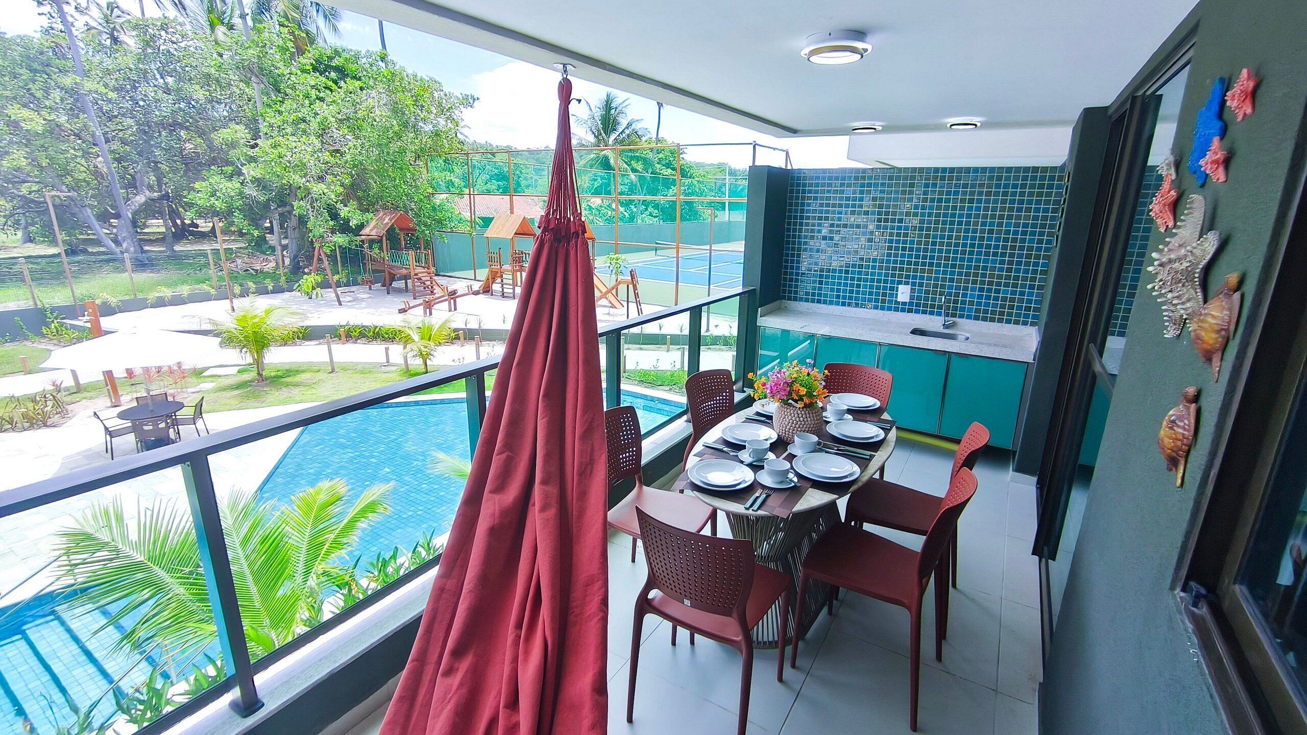 A balcony with a dining table set for four, overlooking a swimming pool and lush greenery.