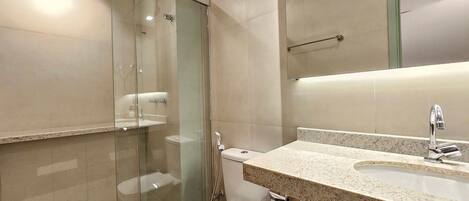 Un baño con ducha de vidrio, inodoro, lavamanos con espejo y perchero para toallas.