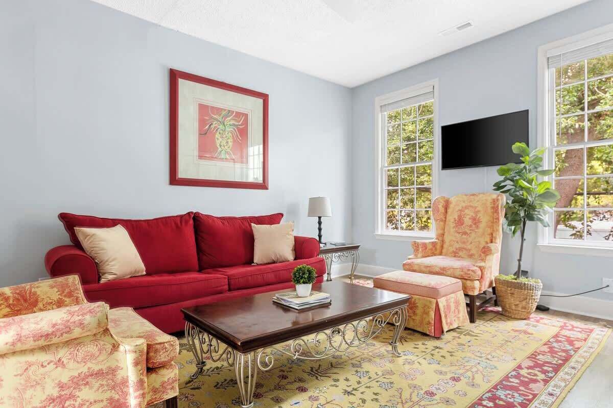 Un salon avec un canapé rouge, un fauteuil assorti, une table basse et une grande fenêtre donnant sur des arbres.