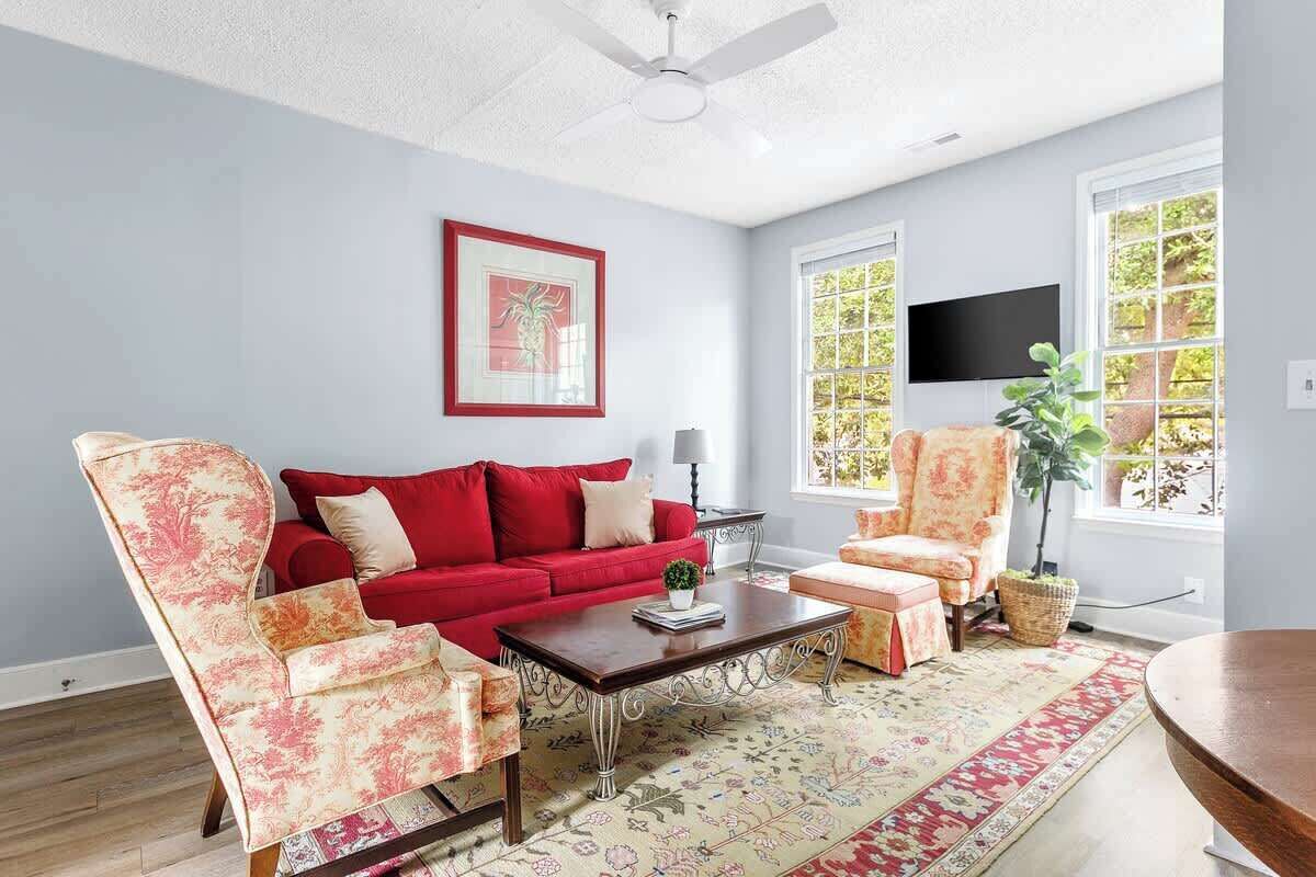 A living room with a red sofa, floral armchairs, a coffee table, and a TV mounted on the wall.
